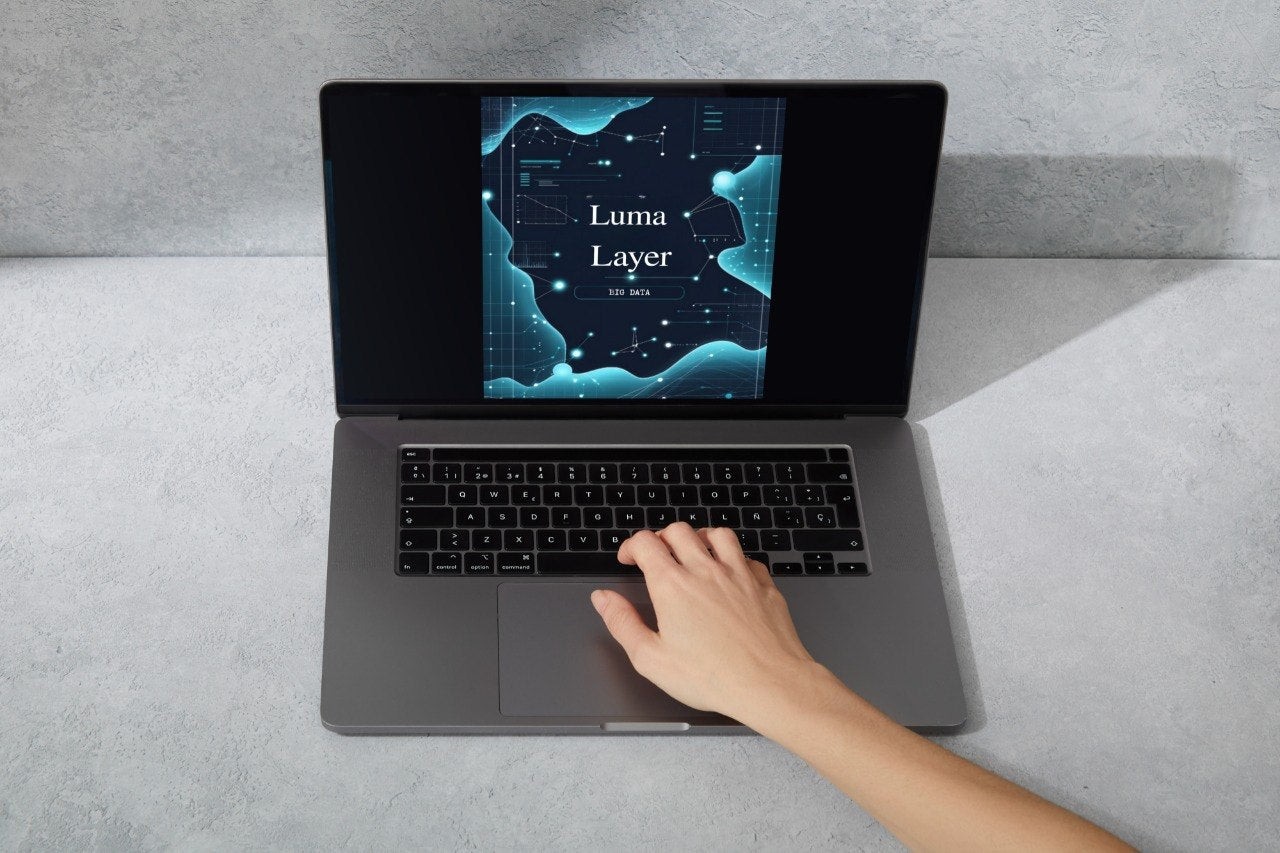 Laptop on a gray surface with a hand interacting with the keyboard, displaying 'Luma Layer' on the screen.